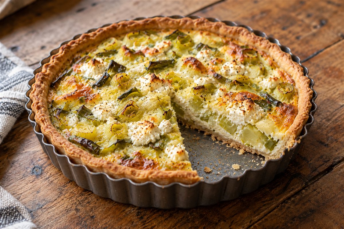 A homemade leek and crumbly white cheese tart in a metal tart tin with one slice cut out
